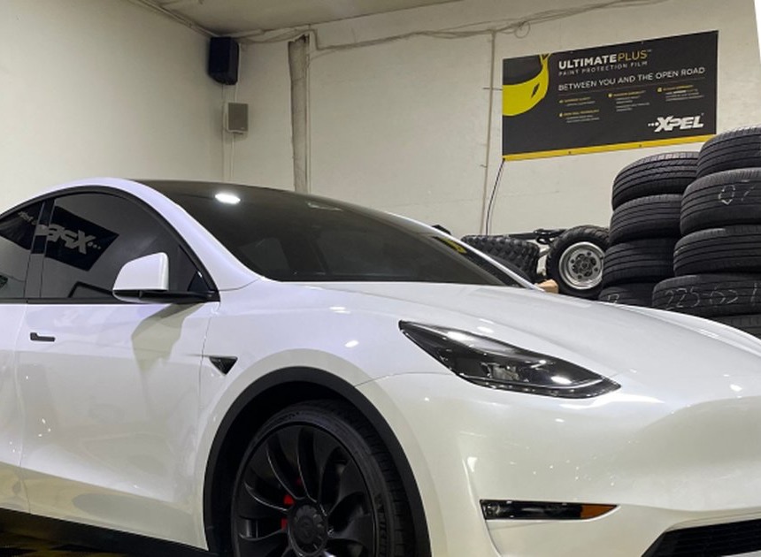 A white Tesla Model Y inside the shop in front of an XPEL paint protection film banner
