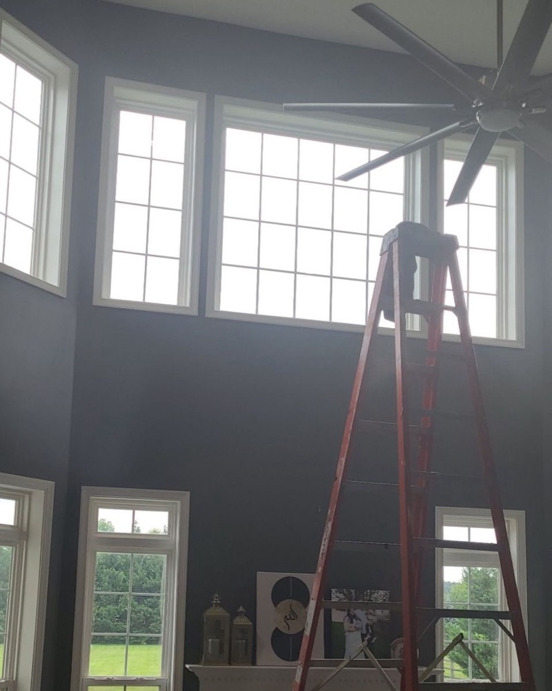 Two-story living room with tall windows being tinted, ladder in place